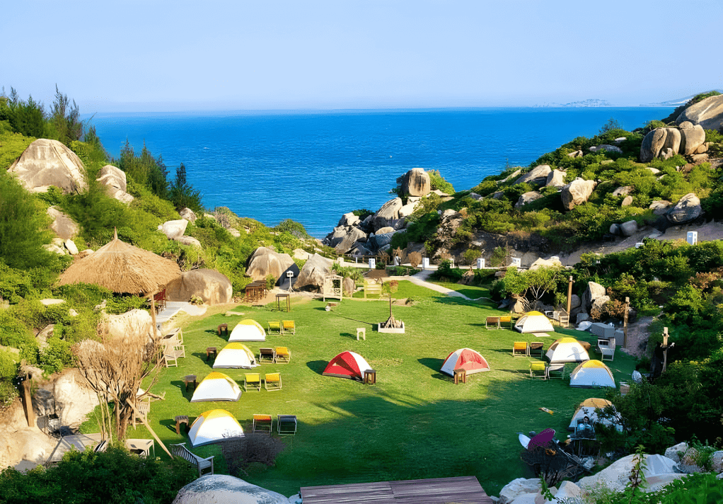 Khu dã ngoại Trung Lương ở Quy Nhơn với lều cắm trại nhiều màu sắc trên bãi biển và khung cảnh núi đá hùng vĩ lúc bình minh