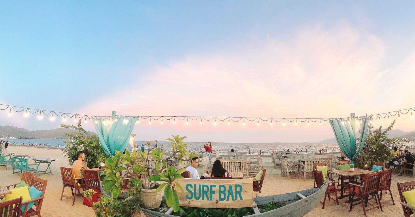 Surf Bar Quy Nhơn buổi tối với ánh đèn lồng lung linh, ghế lười trên cát và du khách thư giãn bên bãi biển